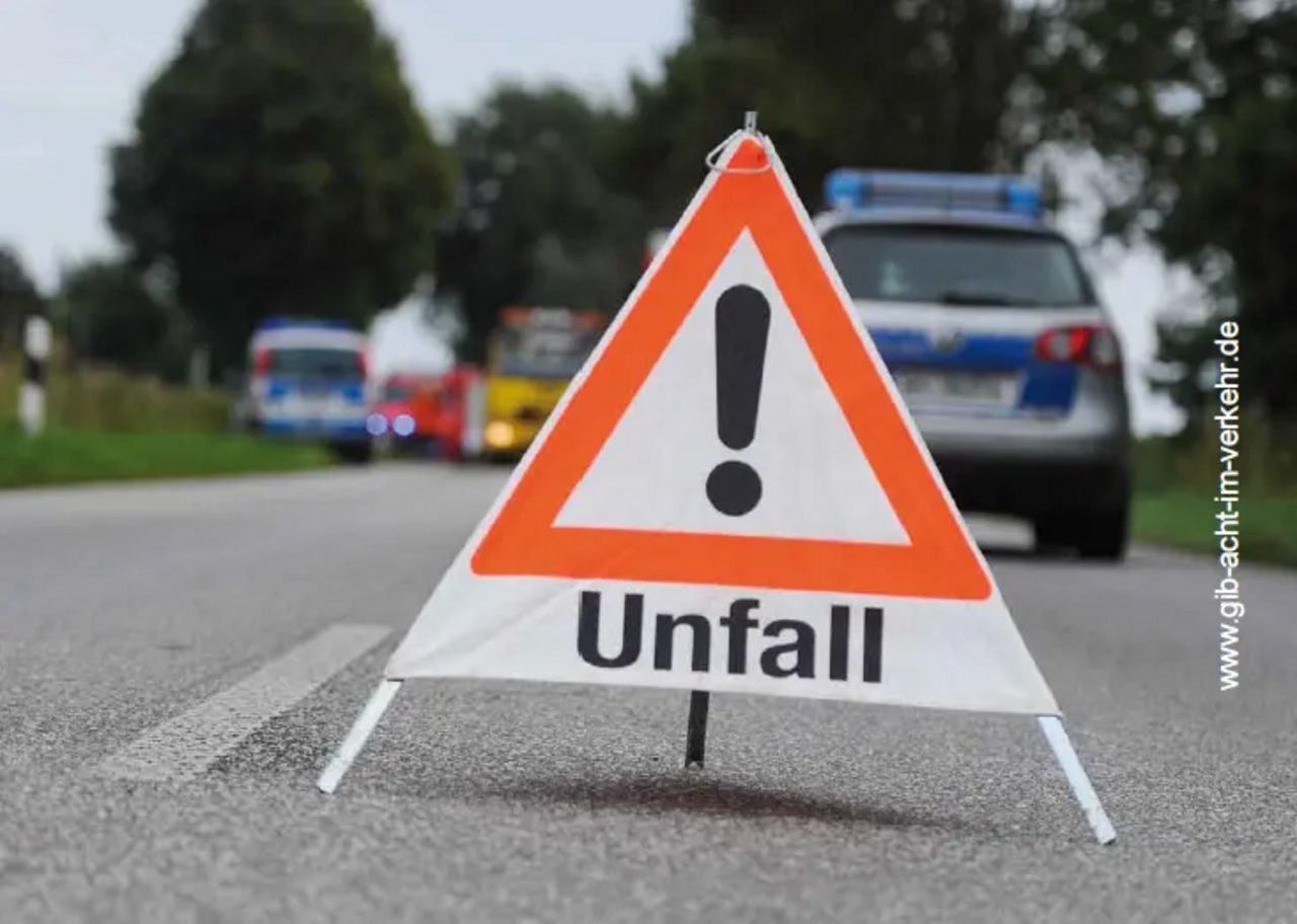 Verkehrsunfall-Warnschild auf einer Straße, im Hintergrund sind Einsatzfahrzeuge zu sehen.