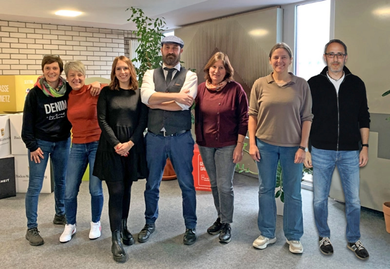 Das KEV-Team 2024 (Koordinierungs- und Entwicklungsstelle Verkehrsunfallprävention). Von links: Carmen-Charlotte Köhler, Martina Musiol, Julia Kraft, Frederik Keegan, Christel Bäuerle, Iris Knaudt (KEV-Leiterin) und Michael Eck. Das Team steht in einem Raum vor einer Wand und lächelt in die Kamera.